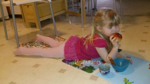 Baby eating apple while lying on placemats on the floor.