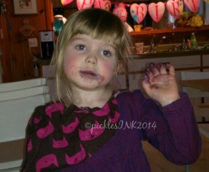 Child with face and fingers stained purple from eating frozen blueberries.