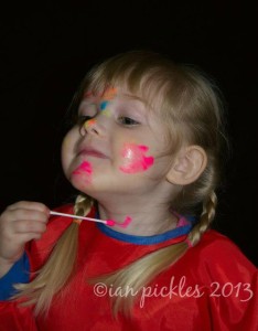 Child smiling and painting her own face.