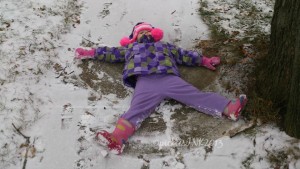 Child making a snow angel in light snow on the sidewalk.